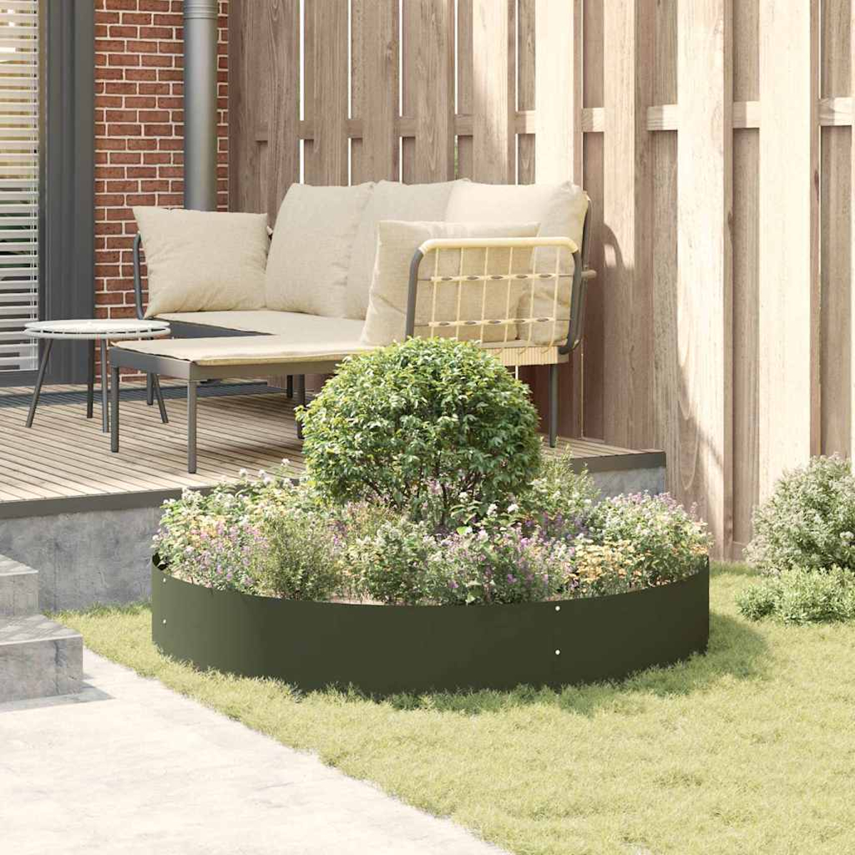 Una scena di giardino con una fioriera circolare verde, un divano beige, una recinzione in legno e un tavolino. Erba e fiori sono visibili.