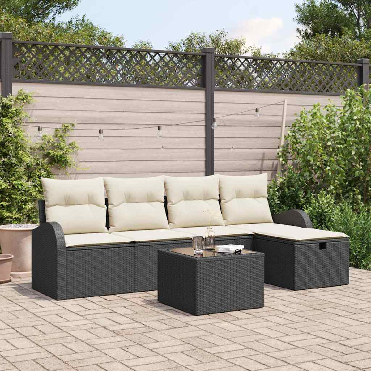 Garten-Terrassenset mit grauem Korbmöbel-Sofa und Tisch. Beige Kissen und Holzzaun im Hintergrund. Ziegelboden.