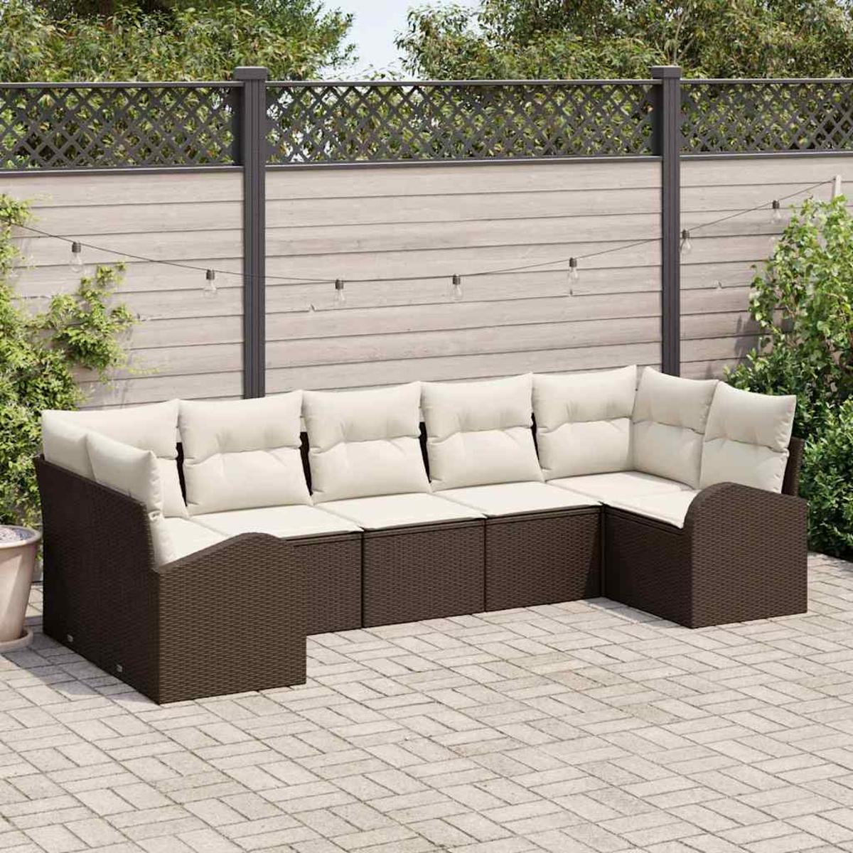 Ein braunes Korbsessel-Sofa mit cremefarbenen Kissen steht auf einer Ziegelterrasse. Ein Zaun und Grünzeug sind im Hintergrund.