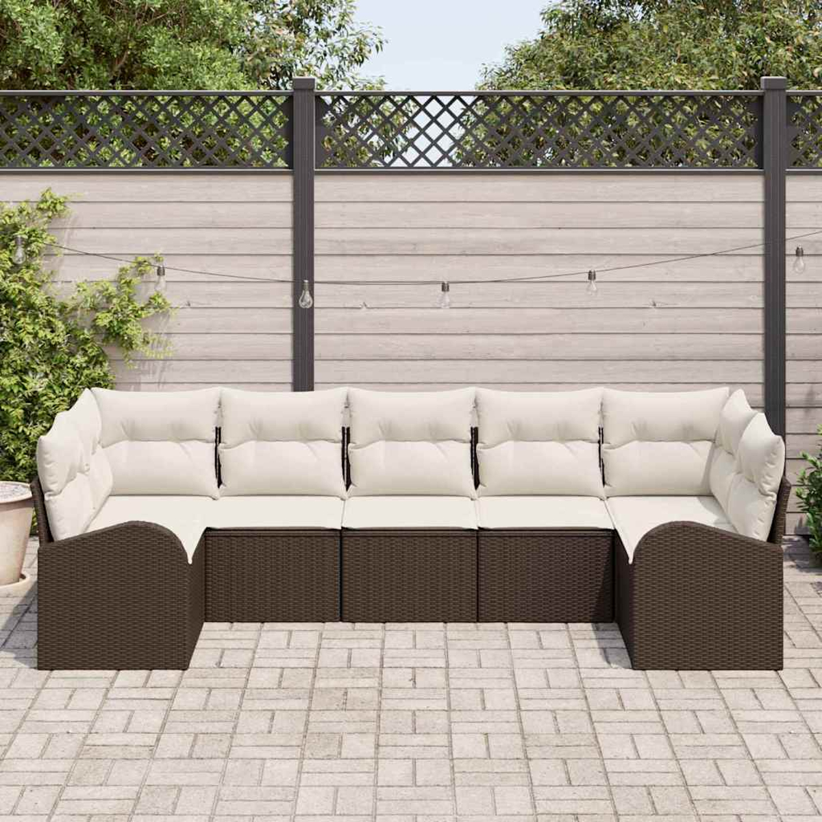 Outdoor-Ecksofa mit cremefarbenen Kissen und braunem Korbbas. Vor einem Holzzaun, Lichterketten und üppigem Grün.