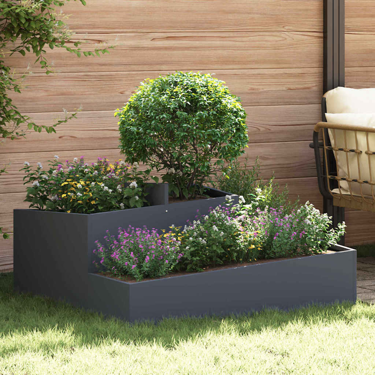 Una fioriera grigio scuro a più livelli con fiori colorati e un cespuglio verde. Una recinzione di legno e una sedia sullo sfondo.