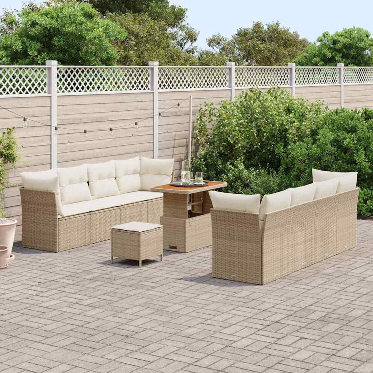 Gartenmöbel-Set. Beige Korbsessel, ein Tisch und ein Hocker auf einer Backstein-Terrasse. Grünes Laub und ein weißer Zaun im Hintergrund.