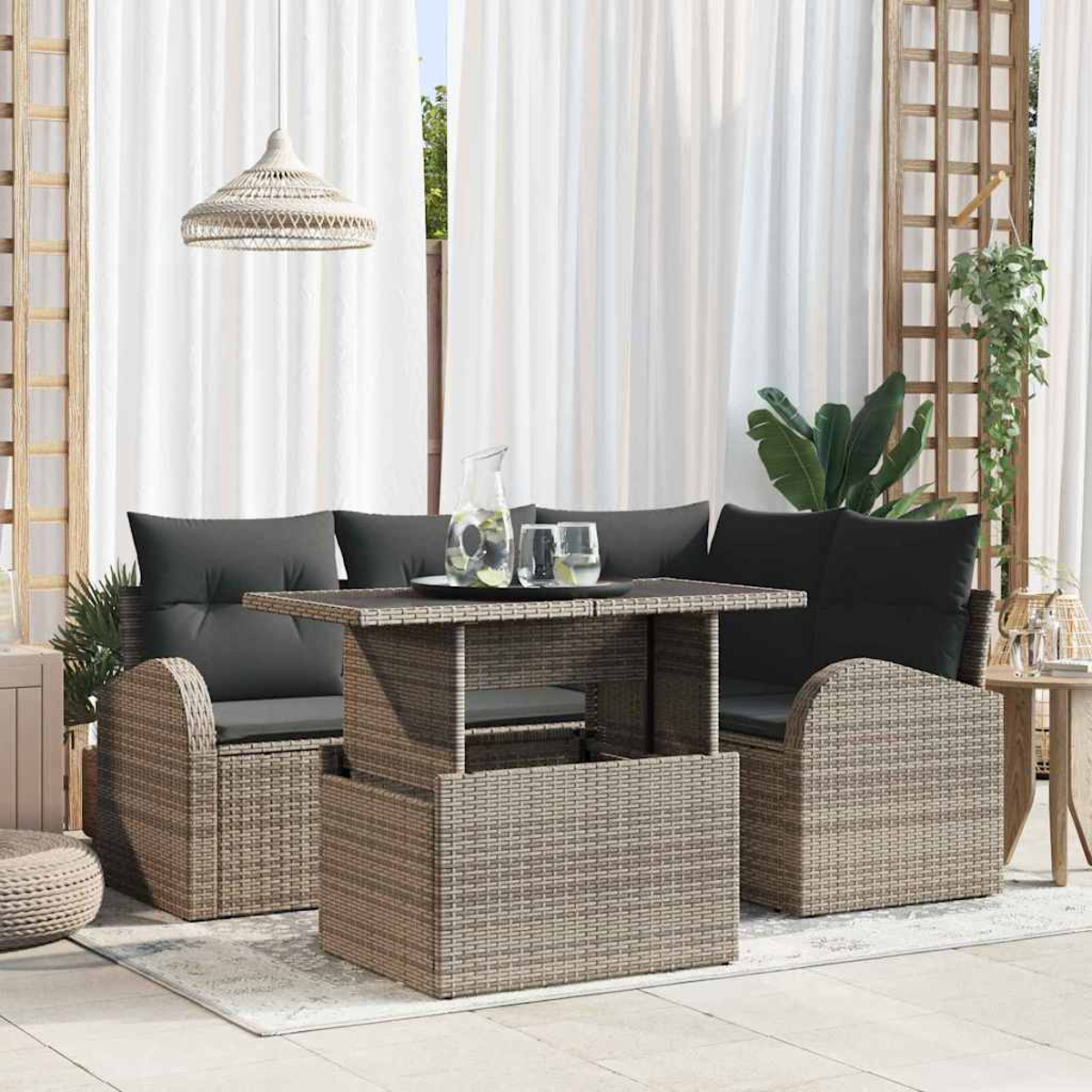 Outdoor-Setting mit Korbmöbeln, Tisch mit Gläsern und einer Hängelampe. Weiße Vorhänge und Pflanzen im Hintergrund.