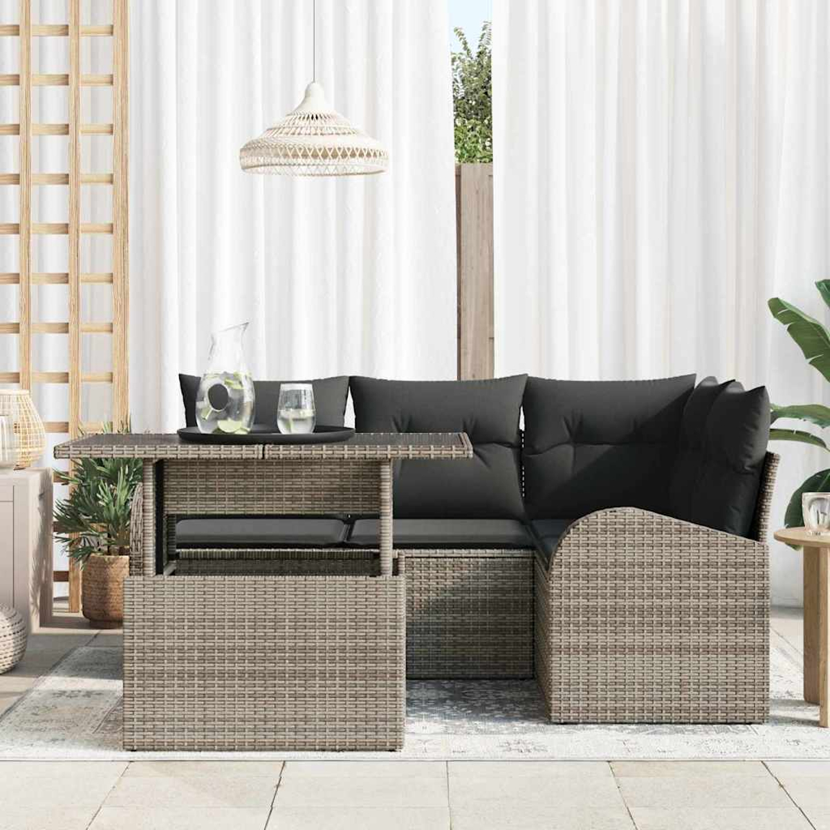 Terrassen-Set mit einem Korbtisch und Sofa. Auf dem Tisch stehen ein Krug und Gläser. Weiße Vorhänge und eine Hängelampe sind zu sehen.