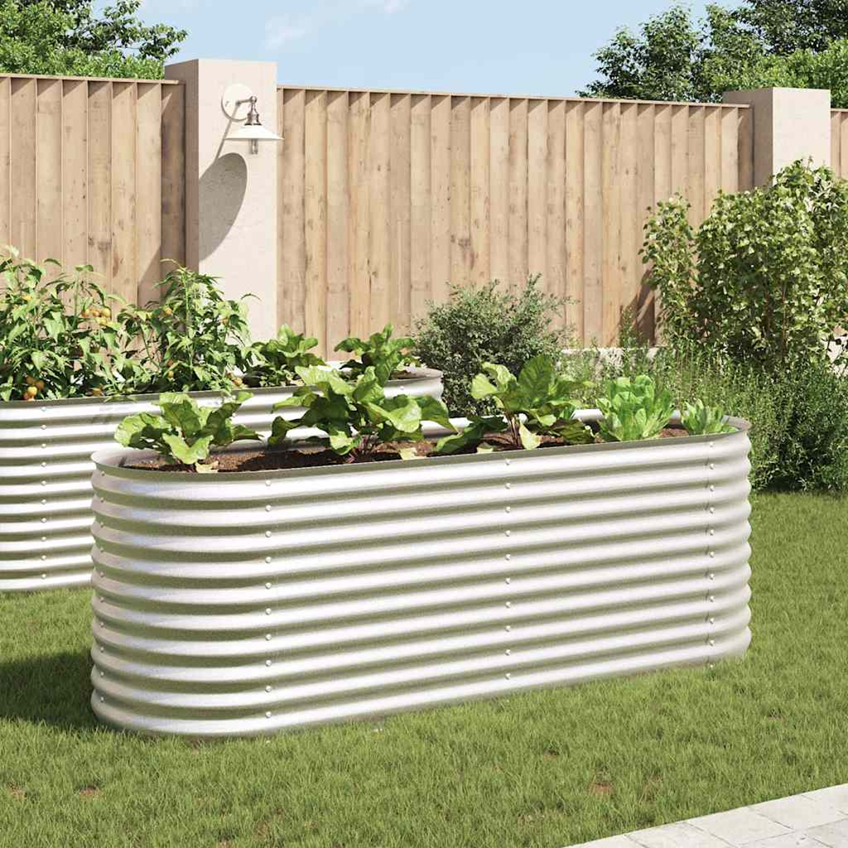 Gemüsegarten mit zwei erhöhten Metallbeeten. Grüne Pflanzen wachsen in den Beeten. Im Hintergrund ein Holzzaun und eine Lampe.