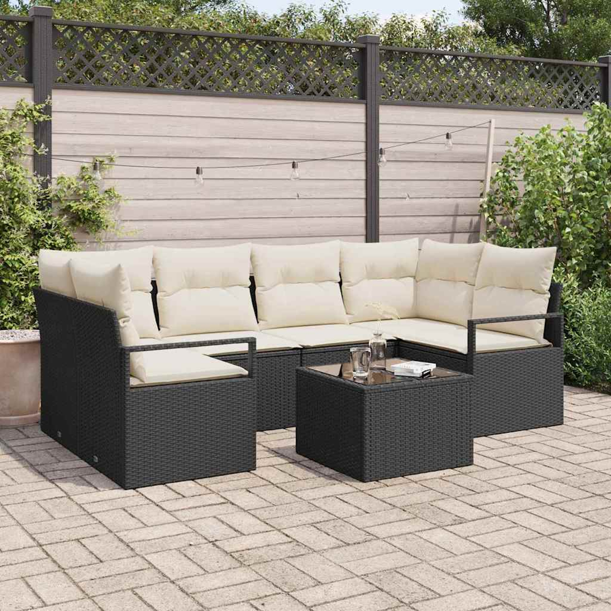 Ein Ecksofa mit cremefarbenen Kissen und einem kleinen Tisch. Im Hintergrund ein Zaun und Pflanzen, darüber Lichterketten.
