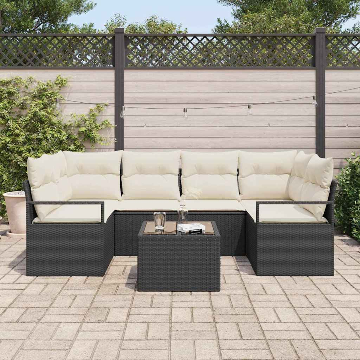 Gartensektionssofa mit cremefarbenen Kissen und einem kleinen Tisch. Auf einer Steinterrasse mit Holzzaun und Grün im Hintergrund.