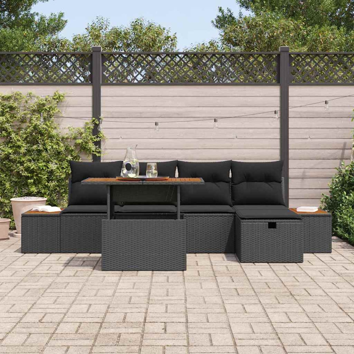 Garten-Terrassenset mit schwarzen Kissen, Tisch und Stauraum. Vor einem Holzzaun und Grün.