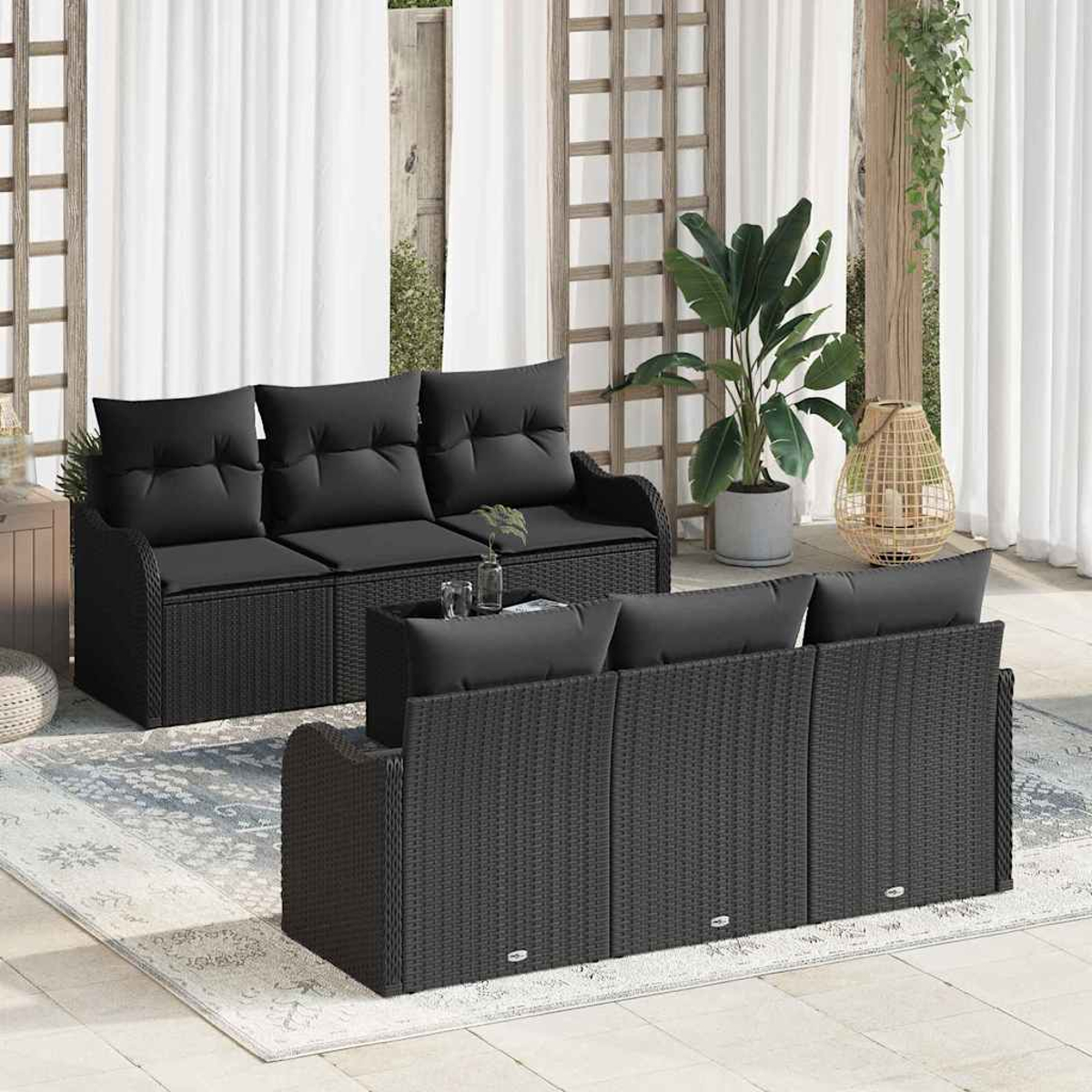 Zwei schwarze Korbs Sofas mit Kissen stehen auf einer Terrasse. Weiße Vorhänge, eine Pflanze und eine dekorative Laterne sind im Hintergrund.