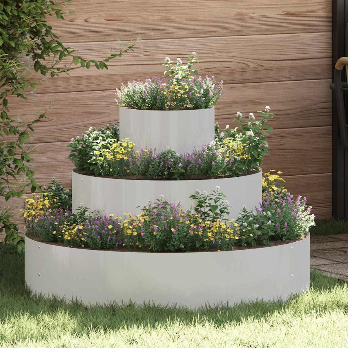 Un'aiuola a più livelli con anelli di metallo bianco. È piena di fiori e vegetazione colorati. Una staccionata di legno è sullo sfondo.