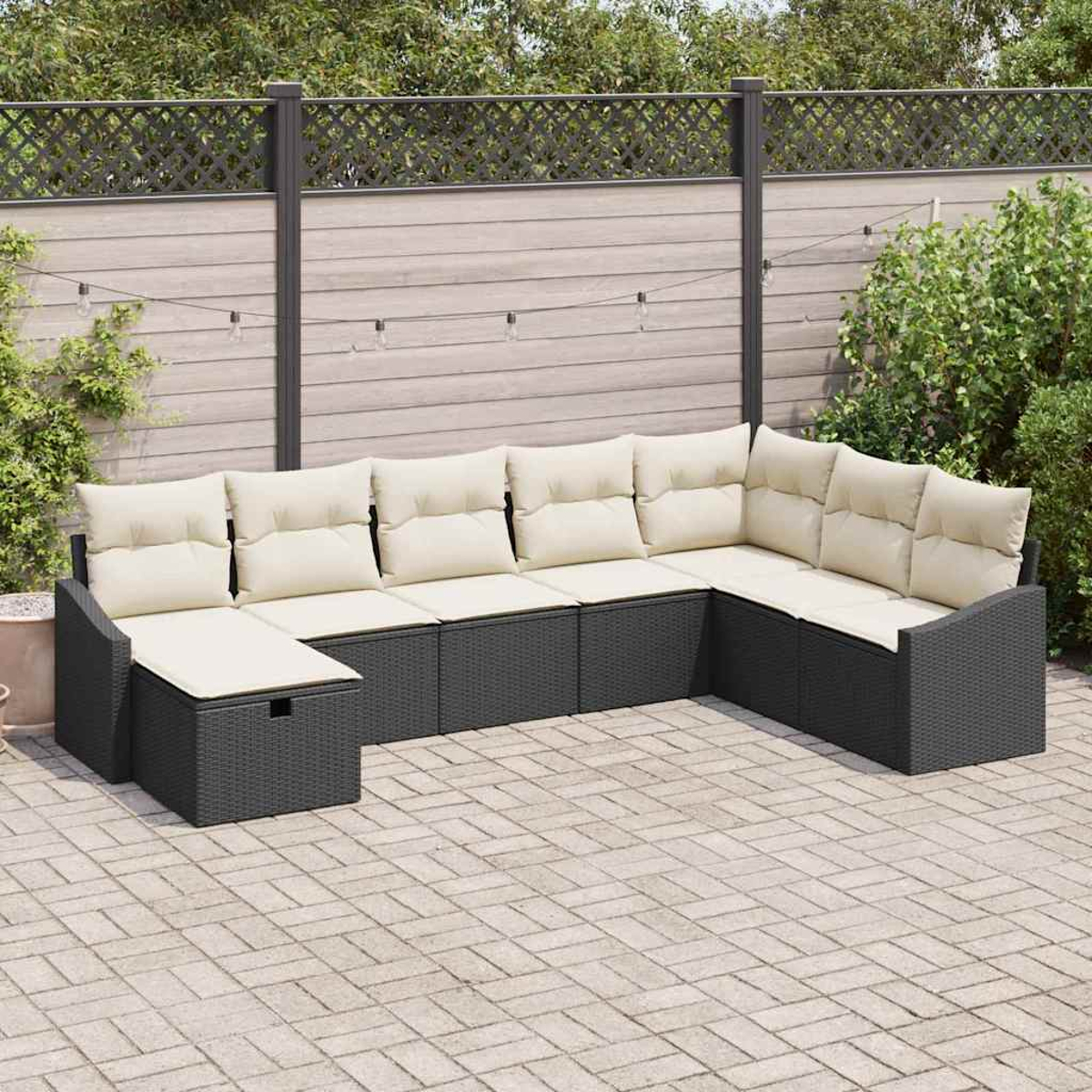Ein U-förmiges, dunkelgraues Outdoor-Sofa mit beigen Kissen steht auf einer Ziegelterrasse. Ein Holzzaun und Laub sind im Hintergrund.
