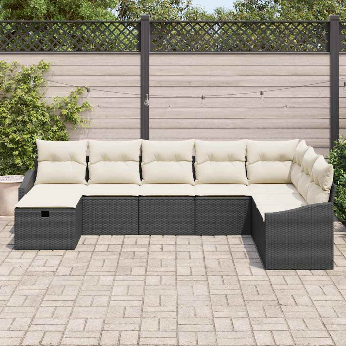 Ein Ecksofa im Freien mit hellen Kissen steht auf einer Ziegelterrasse. Im Hintergrund befinden sich ein Holzzaun und Grün.