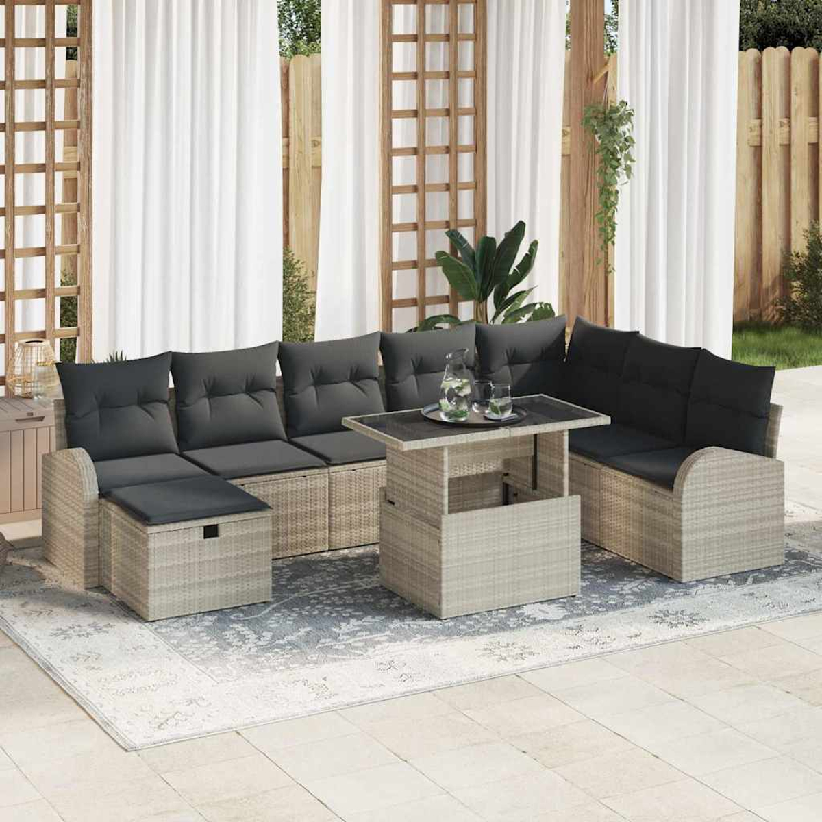 Terrassengarnitur mit grauen Kissen, einem Couchtisch und einem gemusterten Teppich. Vorhänge und ein Holzzaun sind im Hintergrund.