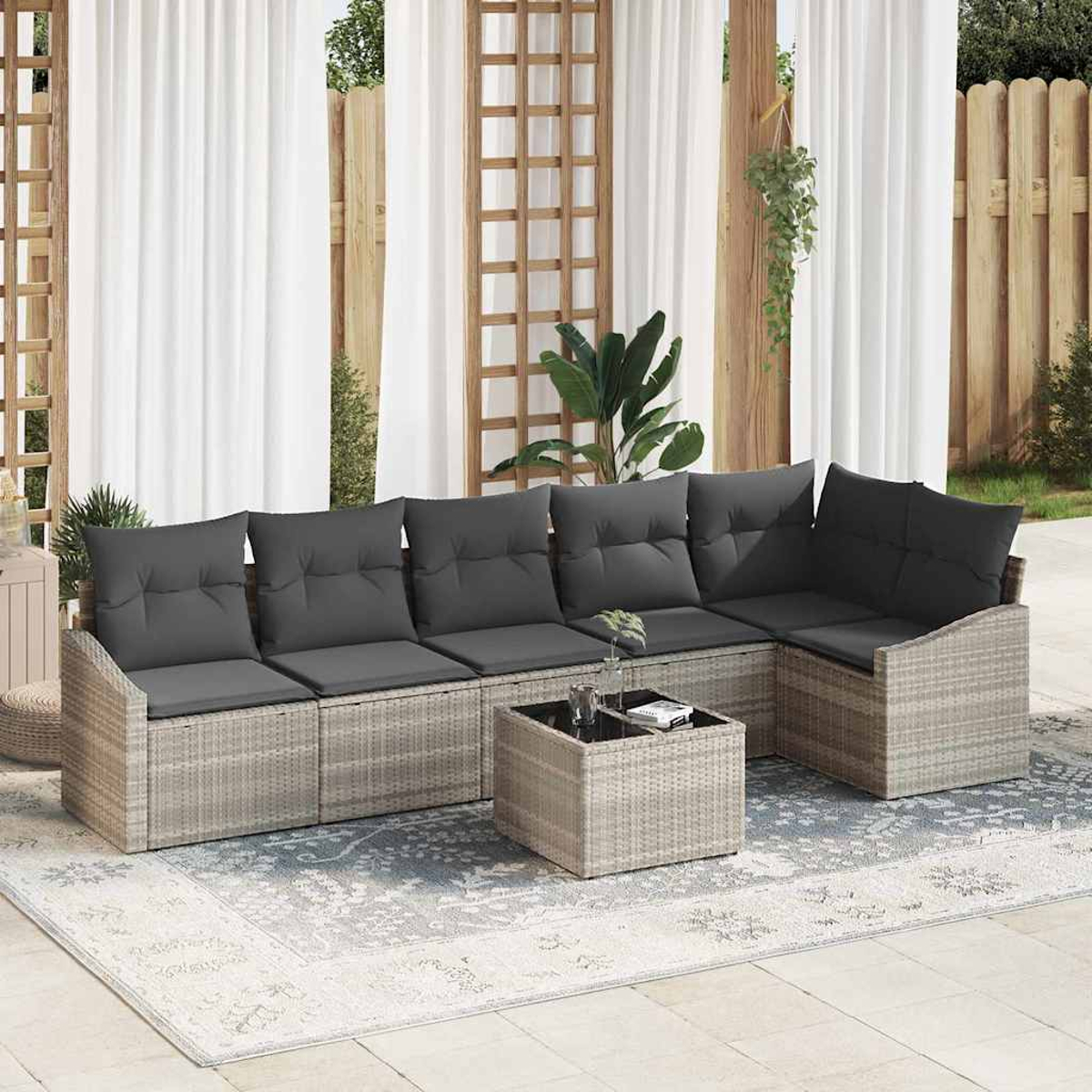 Outdoor-Ecksofa mit grauen Kissen und einem kleinen Tisch. Im Hintergrund ein weißer Vorhang mit Holzdekor und Pflanzen.
