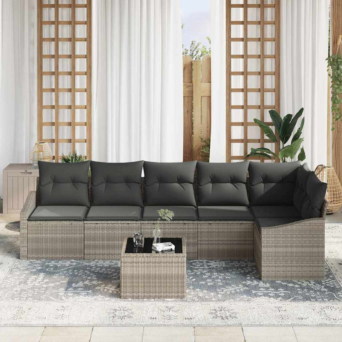 Outdoor-Sitzgruppe mit grauem Ecksofa, Couchtisch und Teppich. Weiße Vorhänge und Holzgitter im Hintergrund.
