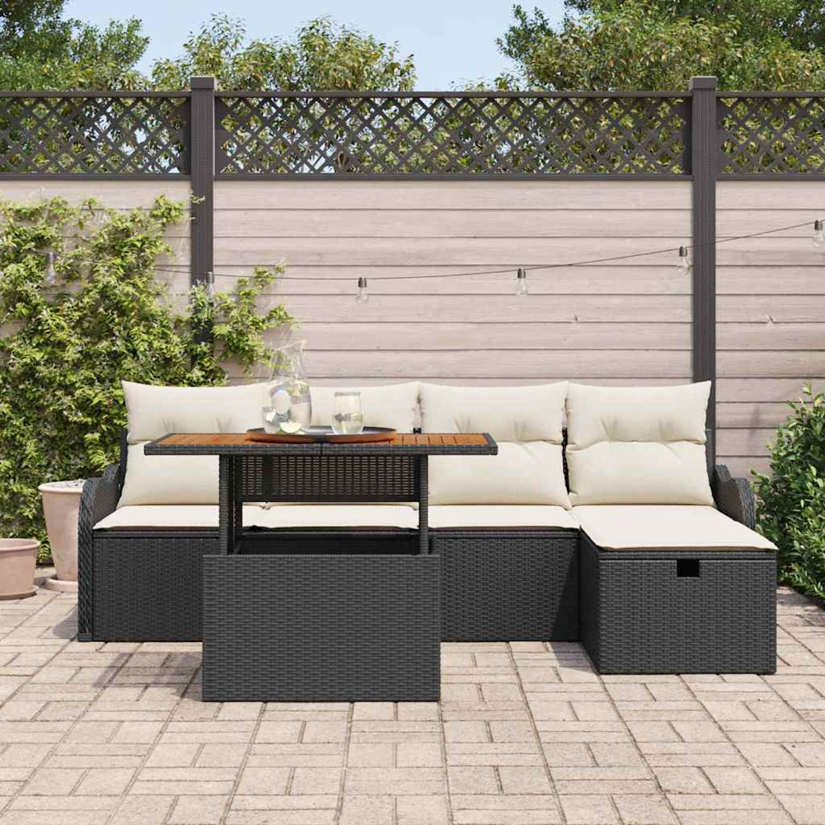 Terrassen-Set mit Tisch, Sofa und Kissen. Im Hintergrund ein dekorativer Zaun. Die Szene spielt sich auf einer Backsteinterrasse ab.