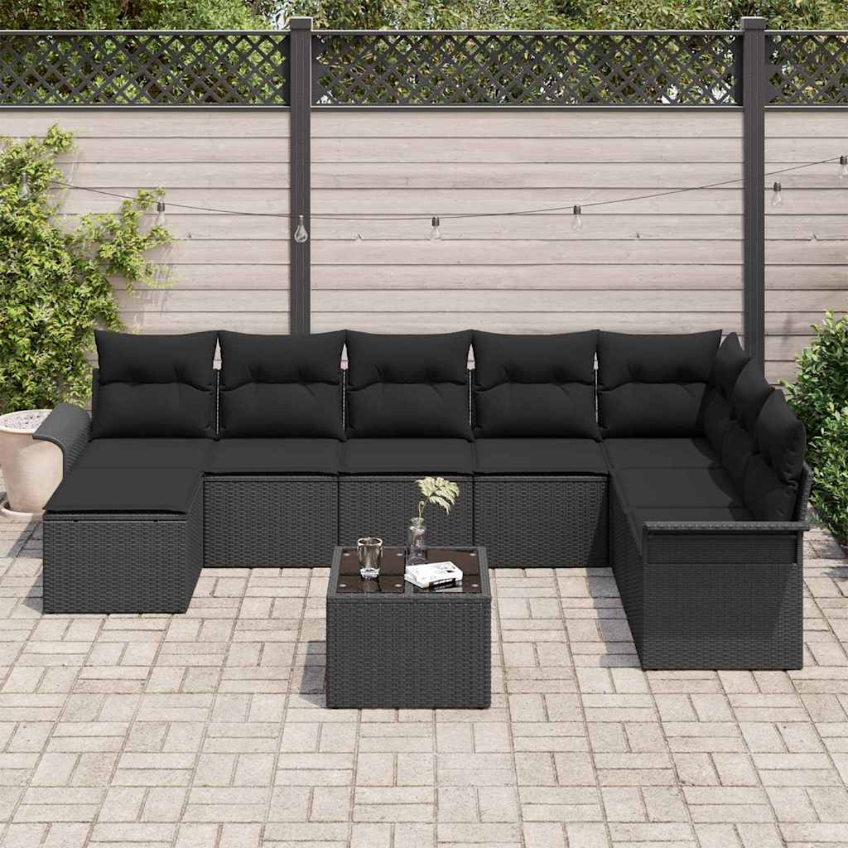 Ein Ecksofa für den Außenbereich mit schwarzen Kissen und einem kleinen Tisch. Im Hintergrund ein Zaun und Grün.