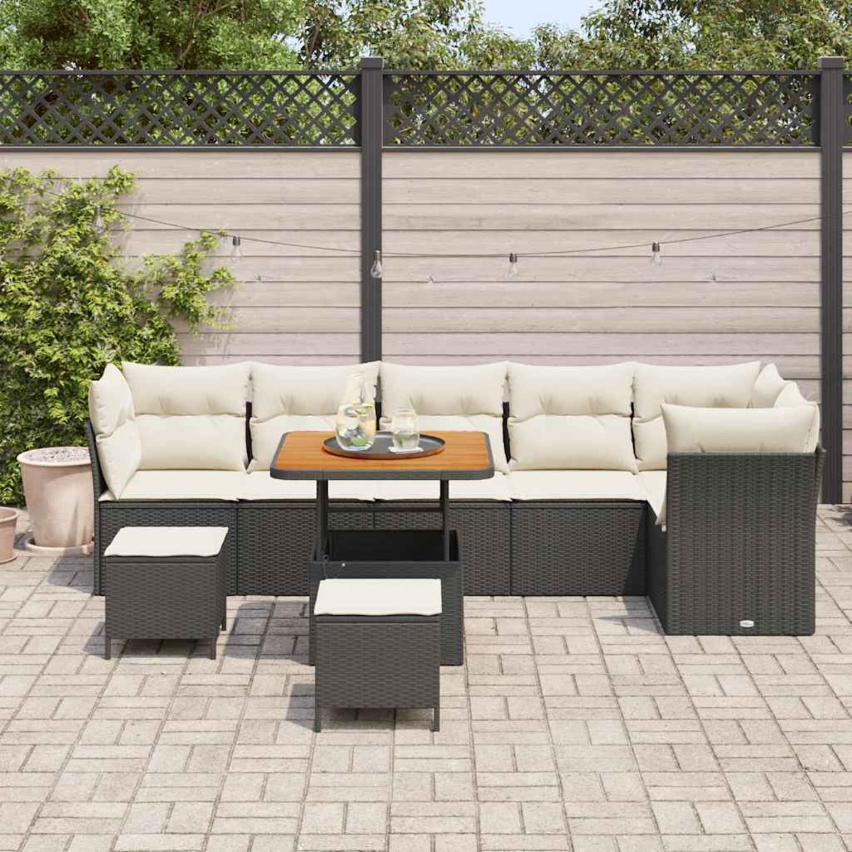 Gartenmöbel-Set mit schwarzer, gewebter Struktur, beigen Kissen und einem kleinen Tisch. Im Hintergrund ein Holzzaun.