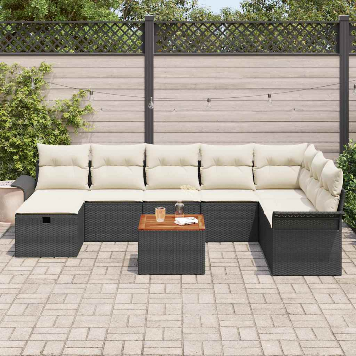 Outdoor-Ecksofa mit cremefarbenen Kissen und einem Holztisch. Auf einer Backstein-Terrasse vor einem Holzzaun und Grün.
