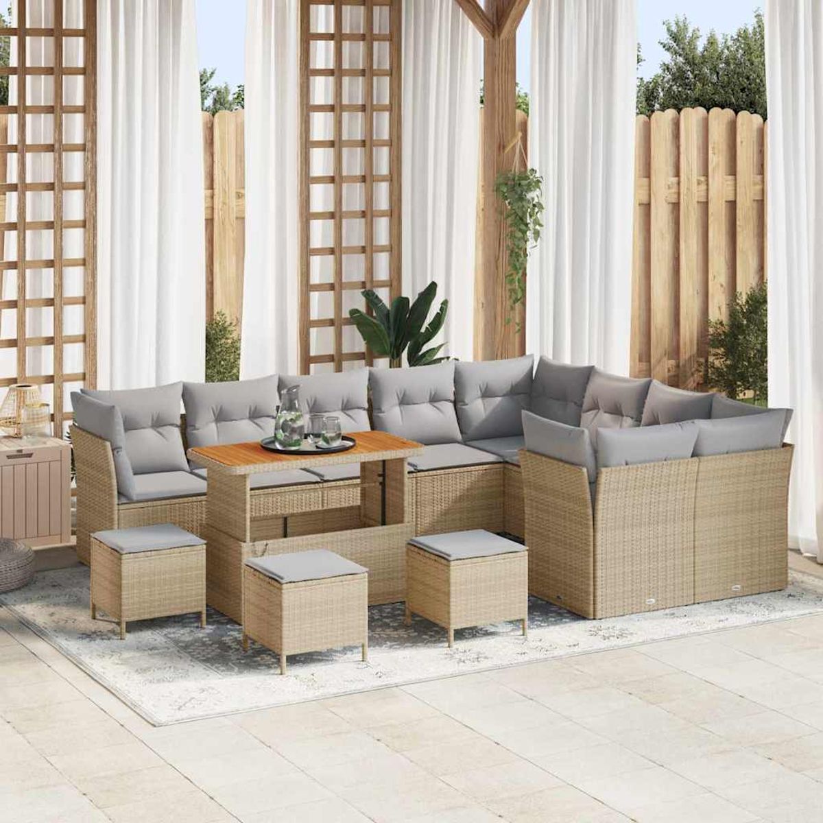 Terrassengarnitur mit grauen Kissen, Holztisch und Hockern. Weiße Vorhänge und Holzzaun im Hintergrund.