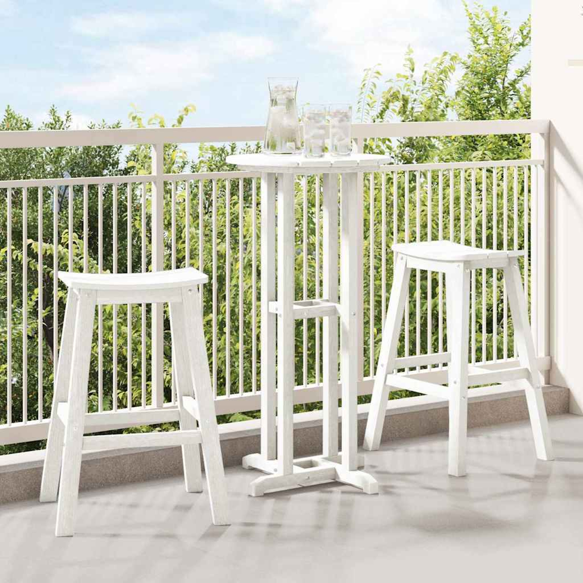 Weißes Outdoor-Bar-Set auf einem Balkon. Beinhaltet einen Tisch mit zwei Hockern und einen Krug mit Gläsern. Grüne Bäume im Hintergrund.