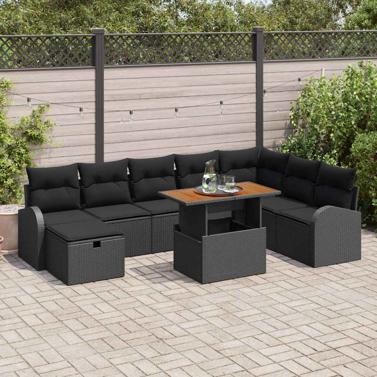 Outdoor-Ecksofa mit schwarzen Kissen und grauem Korbgeflecht. Ein Tisch mit Glas Wasser und Krug. Ein umzäunter Hintergrund.