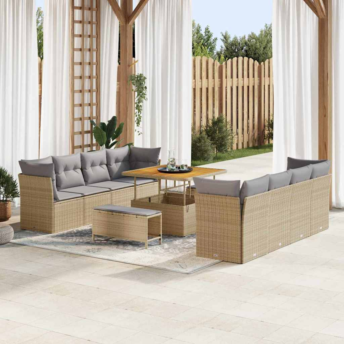 Terrassengarnitur mit Korbmöbeln, grauen Kissen, Holztisch und weißen Vorhängen. Vor dem Sofa befindet sich eine Bank.
