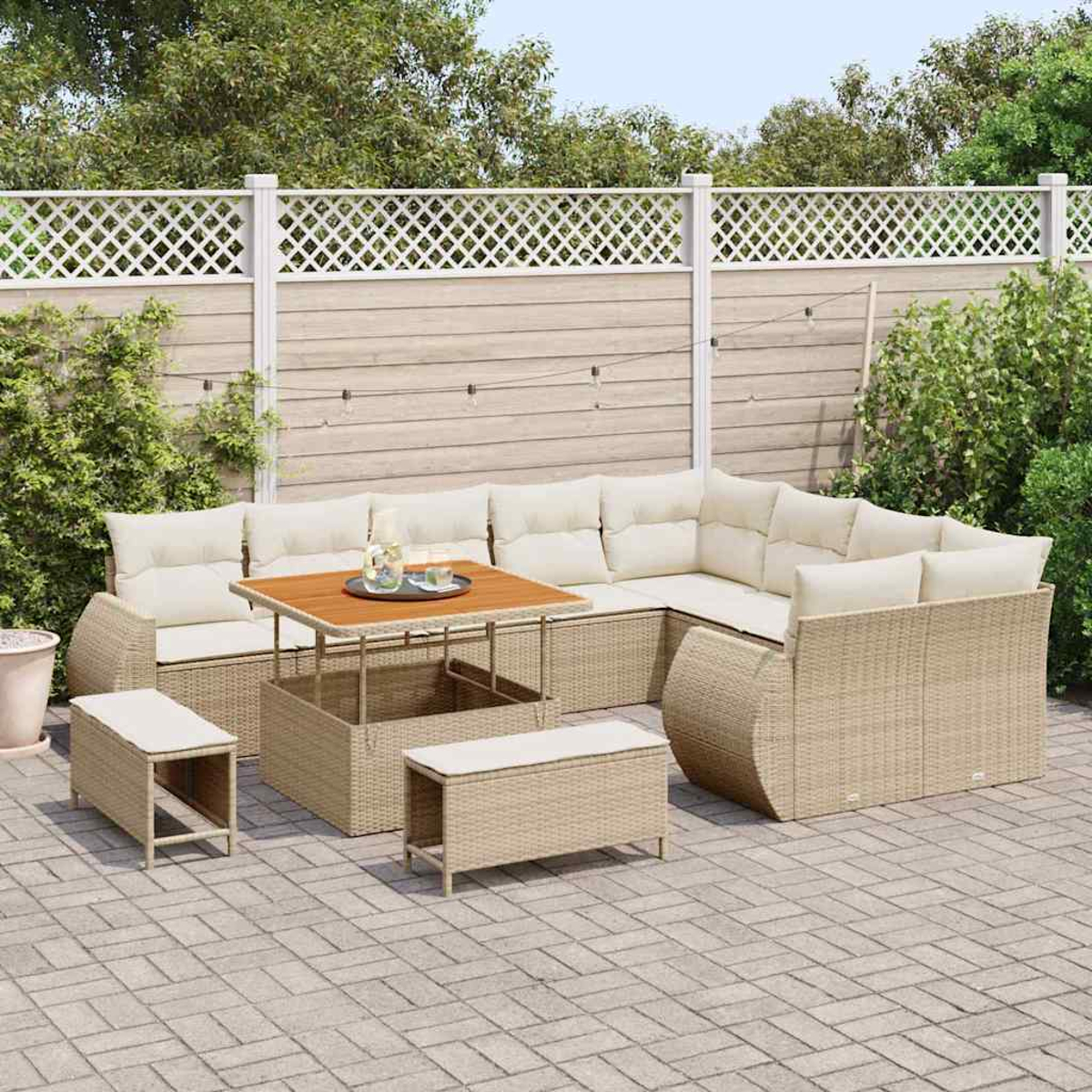 Gartenmöbel-Set. Beigefarbenes Ecksofa aus Korbgeflecht mit Kissen, Couchtisch und zwei Ottomanen auf einer Backstein-Terrasse mit Zaun.