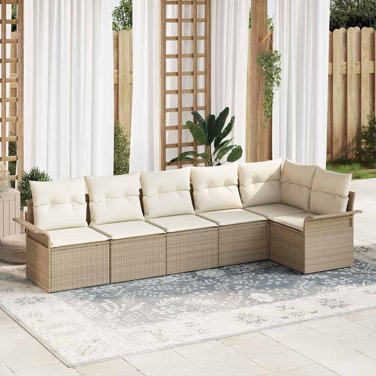 Ein beiges Korbsesselsofa mit cremefarbenen Kissen steht auf einem gemusterten Teppich. Weiße Vorhänge und Holzgitter dahinter.