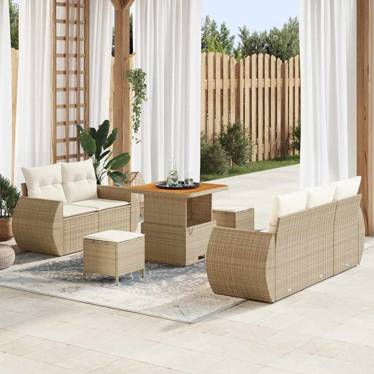 Gartenmöbel-Set auf einer Terrasse. Beinhaltet ein Sofa, zwei Stühle, einen Tisch und zwei Hocker mit weißen Kissen. Holzzaun im Hintergrund.