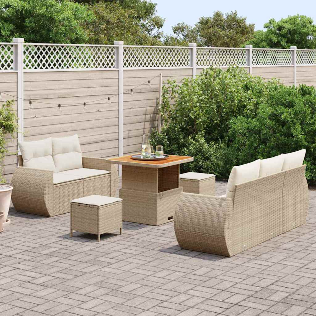 Garten-Terrasseneinrichtung. Rattanmöbel umfassen ein Sofa, zwei Stühle und einen Tisch. Im Hintergrund ein weißer Zaun und üppiges Grün.