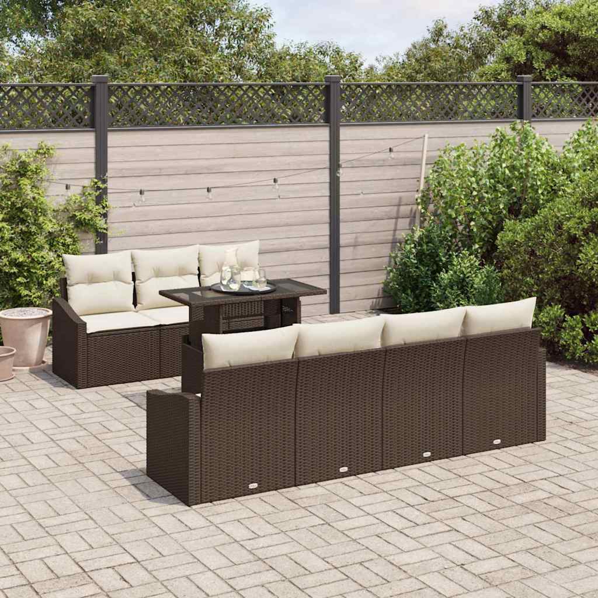 Garten-Terrassenset mit braunen Korbmöbeln und cremefarbenen Kissen. Enthält ein Sofa, eine Liebesbank und einen Tisch auf einer Ziegelpflasterung.