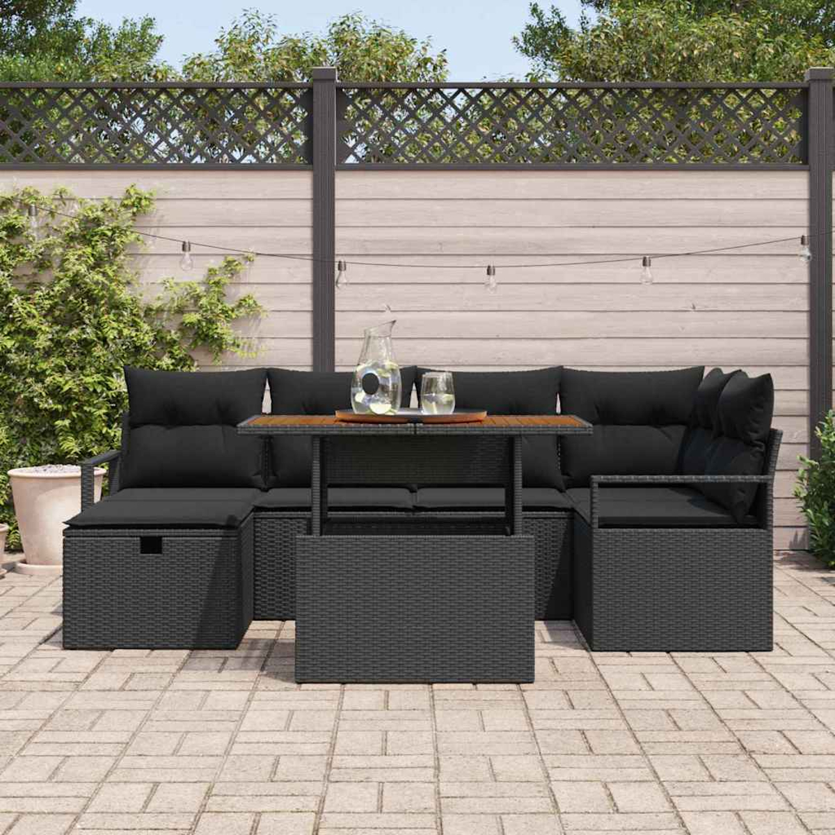 Gartenmöbel-Set. Schwarzes Korbsessel-Sofa mit Kissen, ein Couchtisch und ein Krug mit Gläsern darauf, auf einer Terrasse.