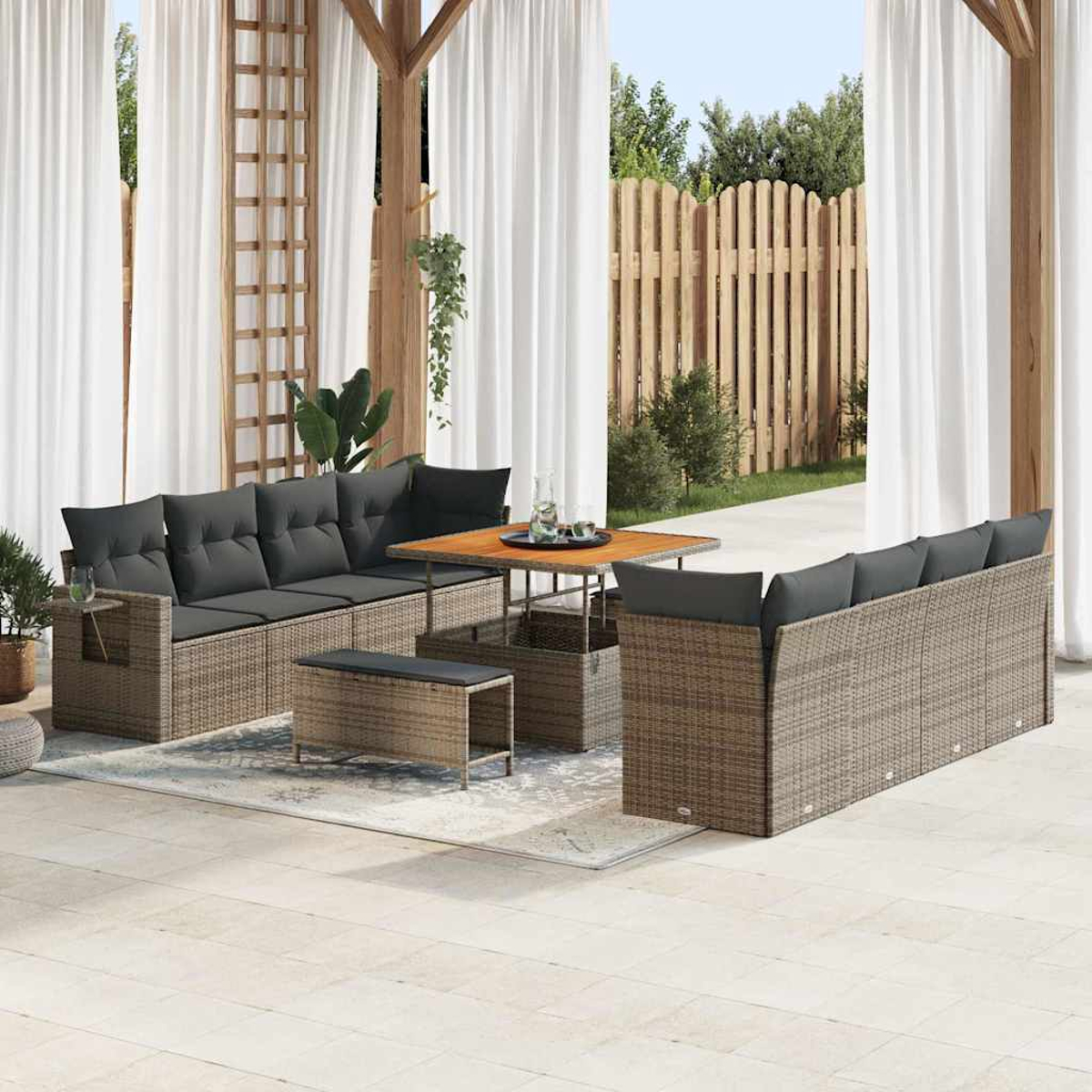 Juego de muebles de mimbre para exteriores en un patio, que incluye sofás, una mesa y un banco. Cortinas blancas y una valla de madera al fondo.