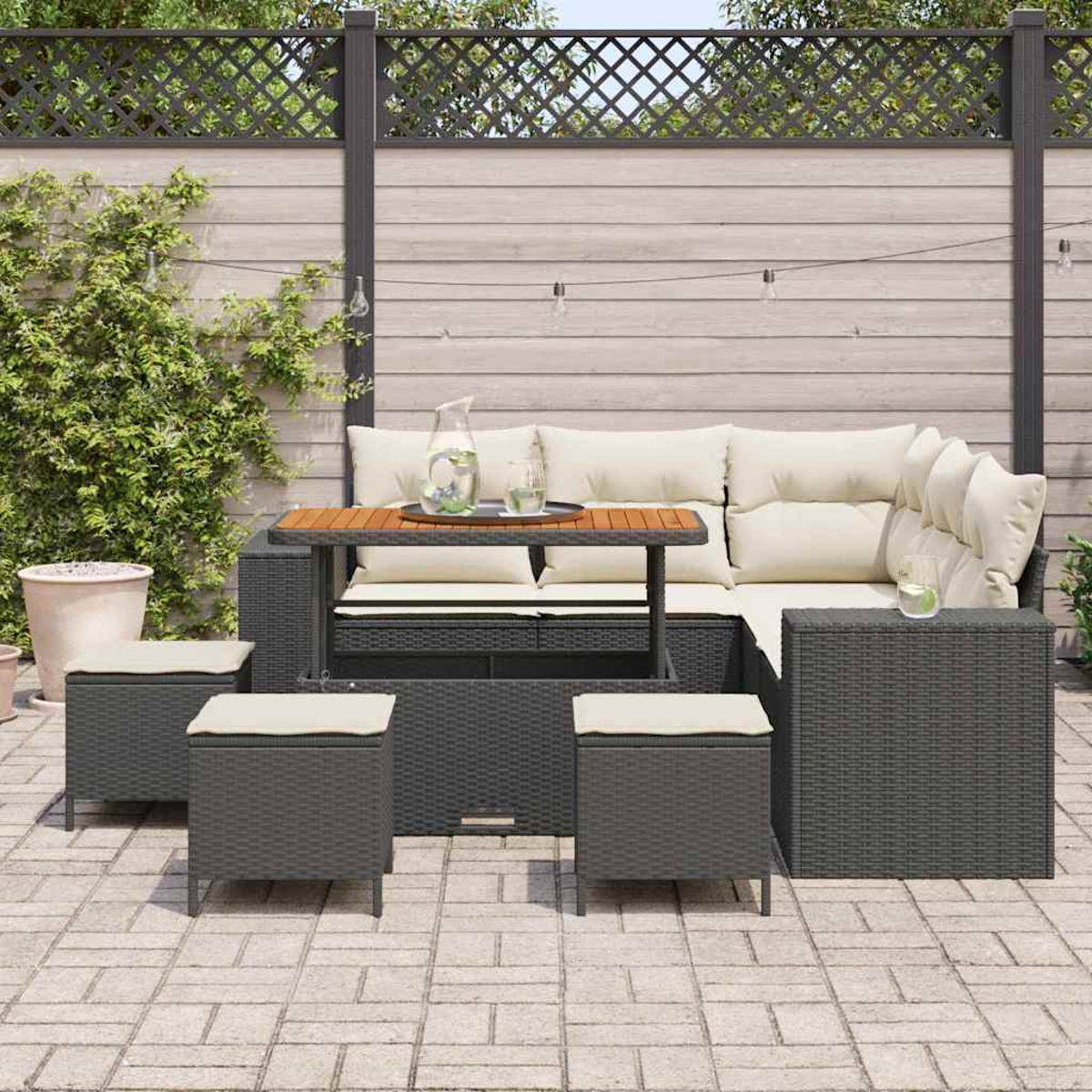 Set da patio esterno con mobili in vimini grigio scuro, cuscini color crema, tavolo in legno e recinzione in legno.