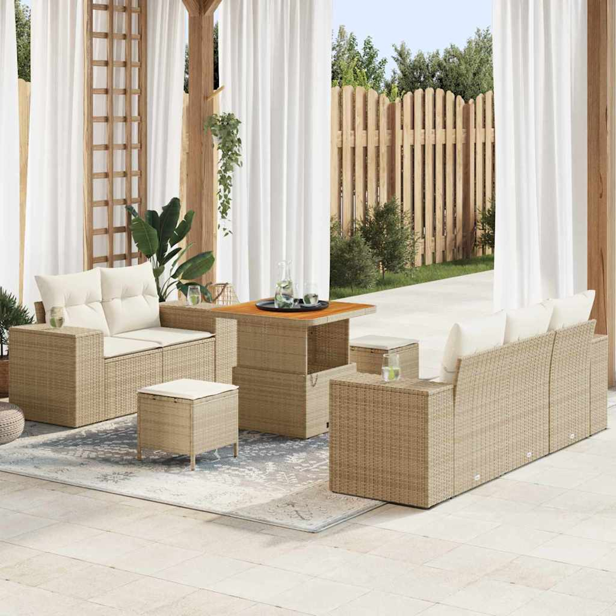 Terrassenset mit beigen Rattanmöbeln, weißen Kissen, Tisch und Vorhängen. Im Hintergrund ein Holzzaun.