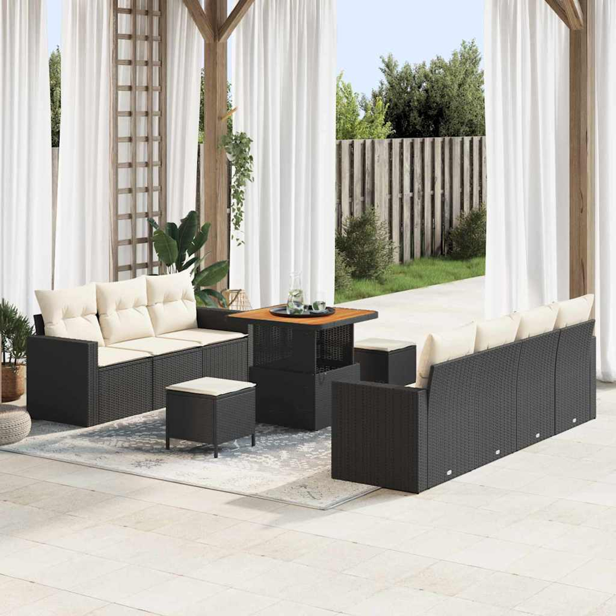 Terrassenset im Freien mit schwarzen Korbsesseln, beigen Kissen, Holztisch und einem Teppich. Weiße Vorhänge und ein Garten im Hintergrund.