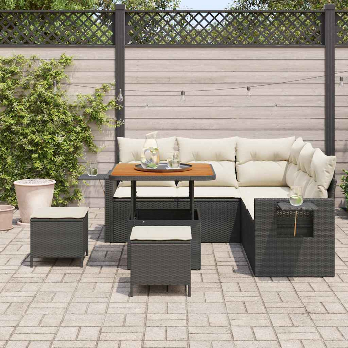 Set di sedute per esterni con divano angolare, tavolo e sgabelli. Il set è su un patio, con una staccionata in legno e piante rampicanti.