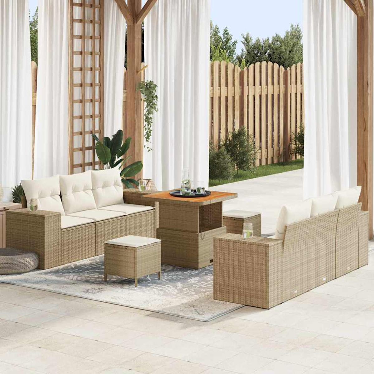 Terrassenset mit Korbs Sofas, Tisch und Ottomanen. Weiße Vorhänge und Holzzaun im Hintergrund.