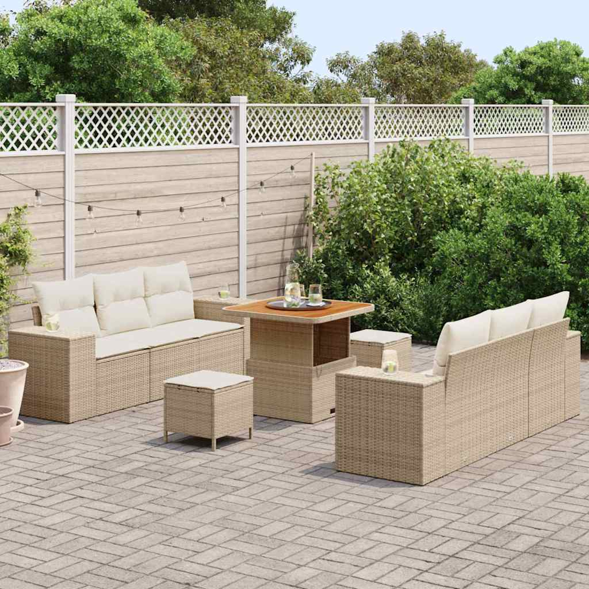 Terrassenset im Freien mit beigefarbenen Korbsesseln, einem Tisch und Hockern auf einer Backsteinterrasse. Ein weißer Zaun und Grün bilden den Hintergrund.