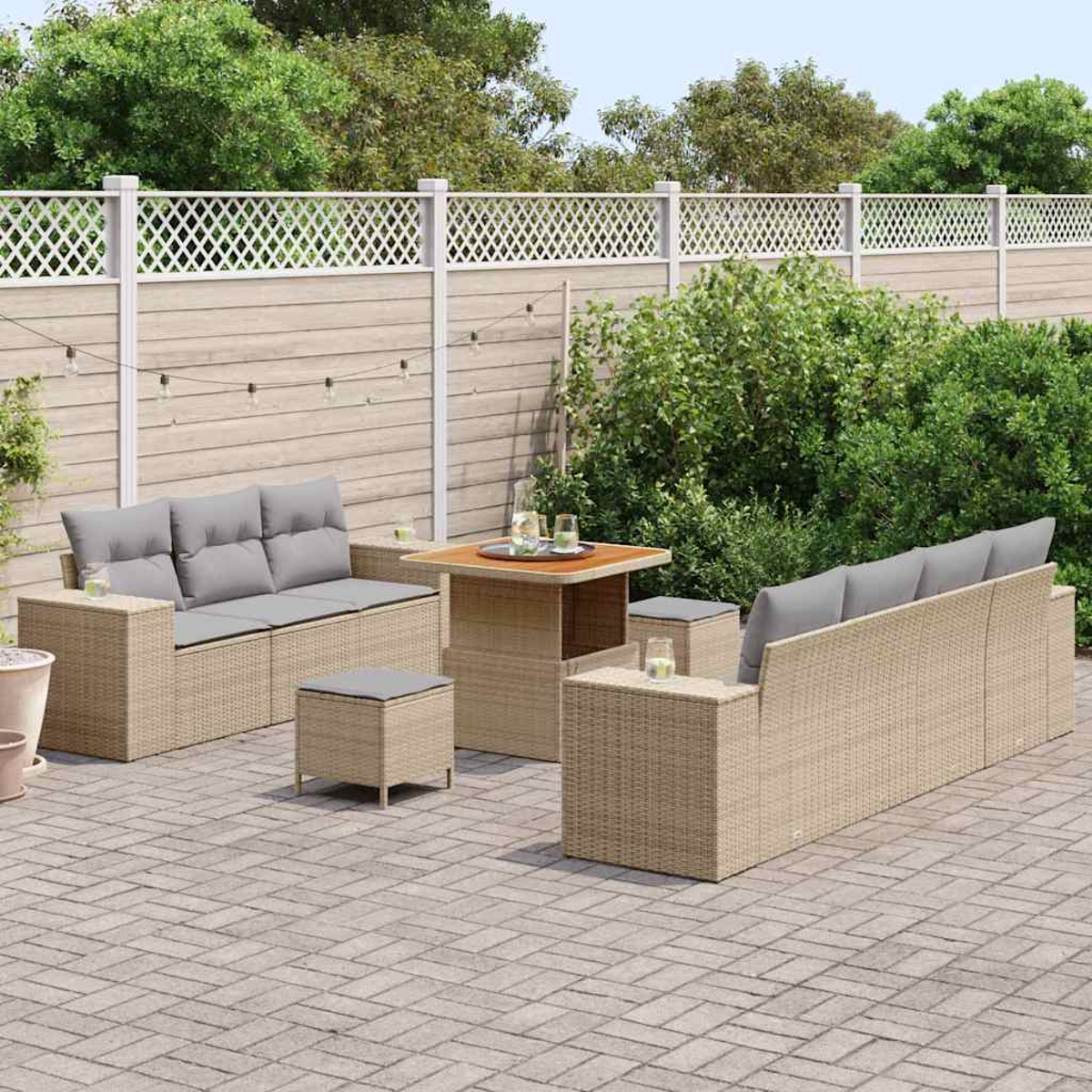 Gartenmöbel-Set. Beige Korbsessel und Tische auf einer Backstein-Terrasse. Grüne Büsche und ein weißer Zaun im Hintergrund.