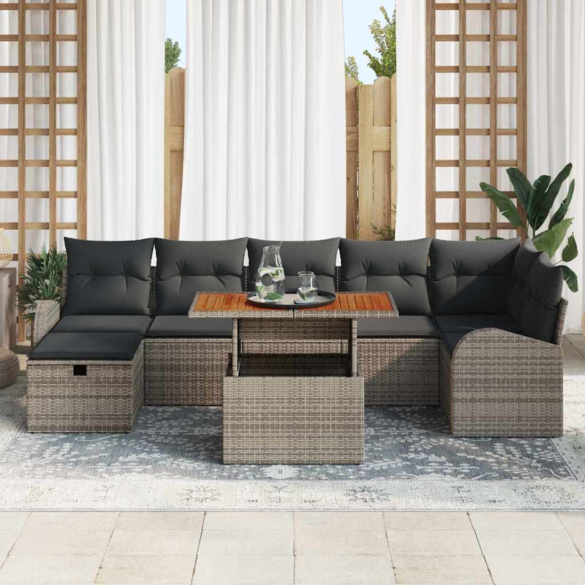 Graues Outdoor-Ecksofa mit schwarzen Kissen, einem Holztisch mit Getränken und weißen Vorhängen im Hintergrund.