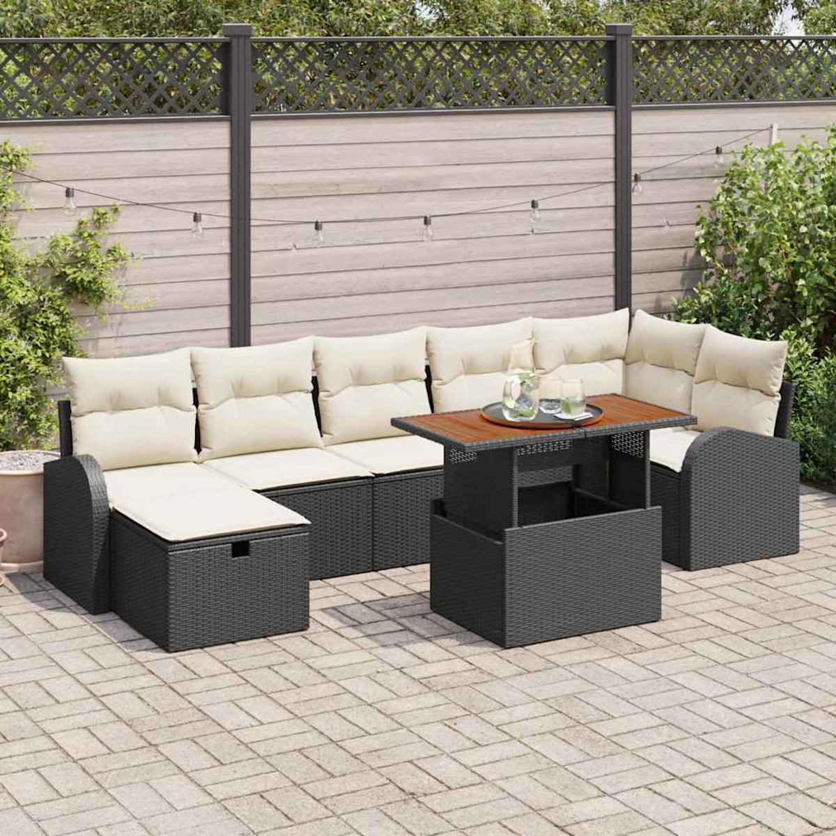 Terrassenmöbel mit beigen Kissen und einem Holztisch auf einer gepflasterten Terrasse. Im Hintergrund sind Zaun und Grün zu sehen.