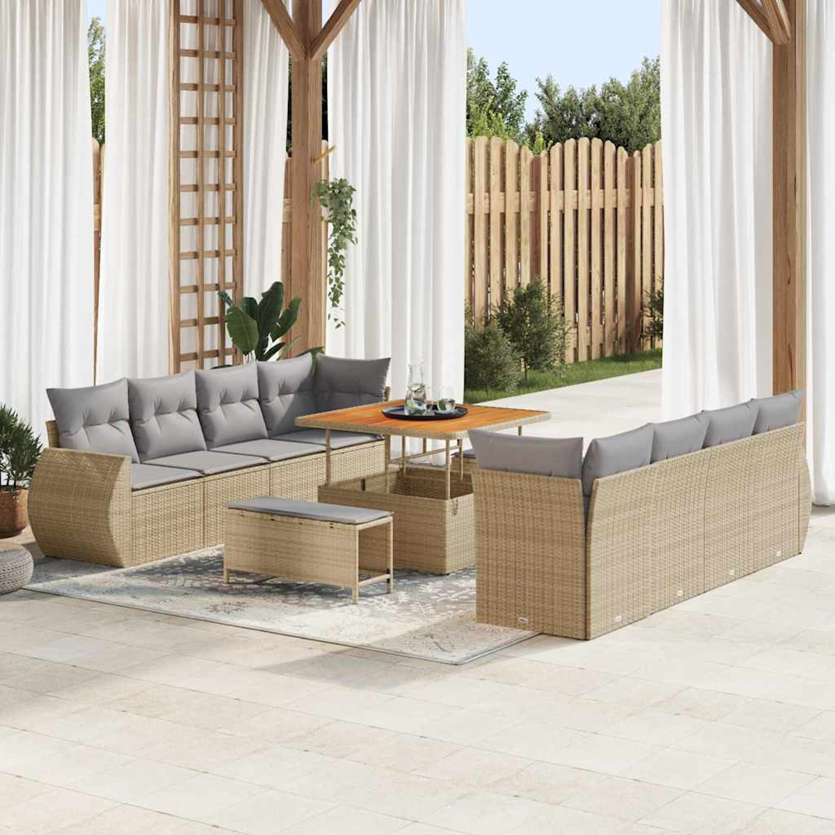 Garten-Terrassenset mit hellbraunen Korbmöbeln, grauen Kissen, Holztisch und weißen Vorhängen. Im Hintergrund ein Holzzaun.