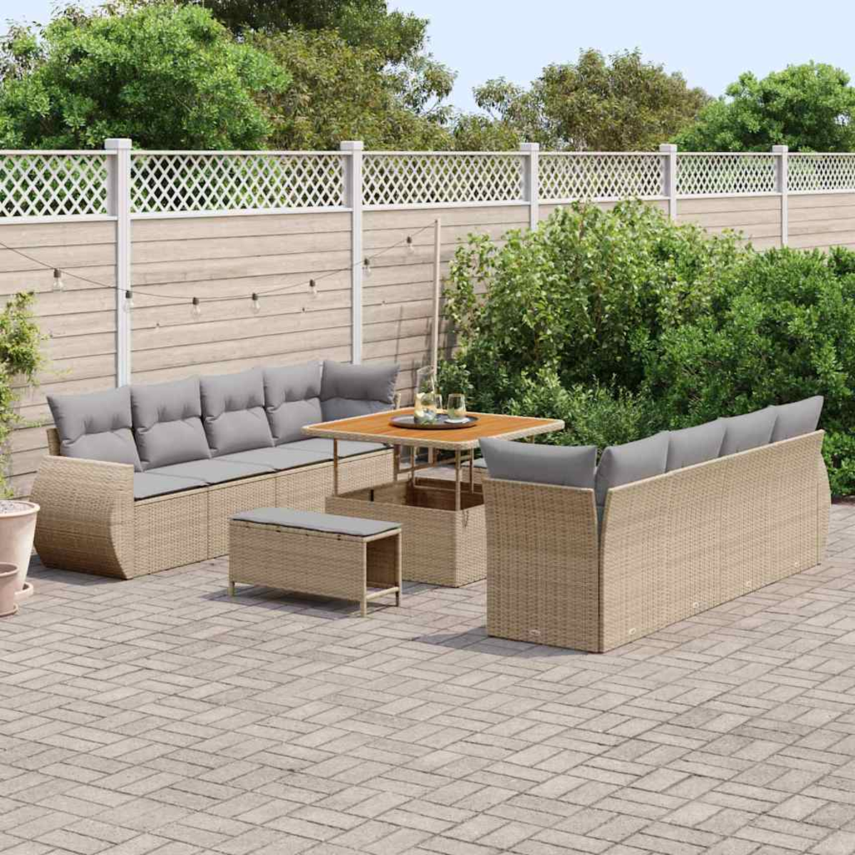 Ein Terrassenset mit Korbmöbeln und grauen Kissen. In der Mitte steht ein Tisch mit Gläsern, umgeben von Grün und einem Zaun.