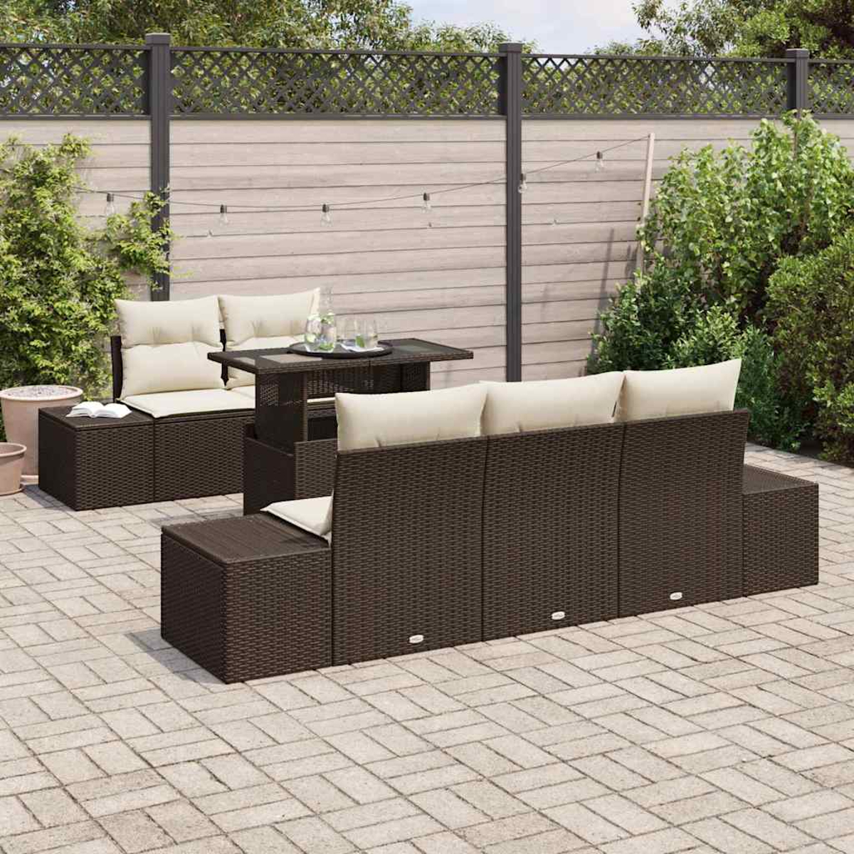 Ein braunes Outdoor-Möbelset aus Korbgeflecht auf einer Ziegelterrasse. Das Set umfasst ein Sofa, Stühle und einen Tisch mit cremefarbenen Kissen.