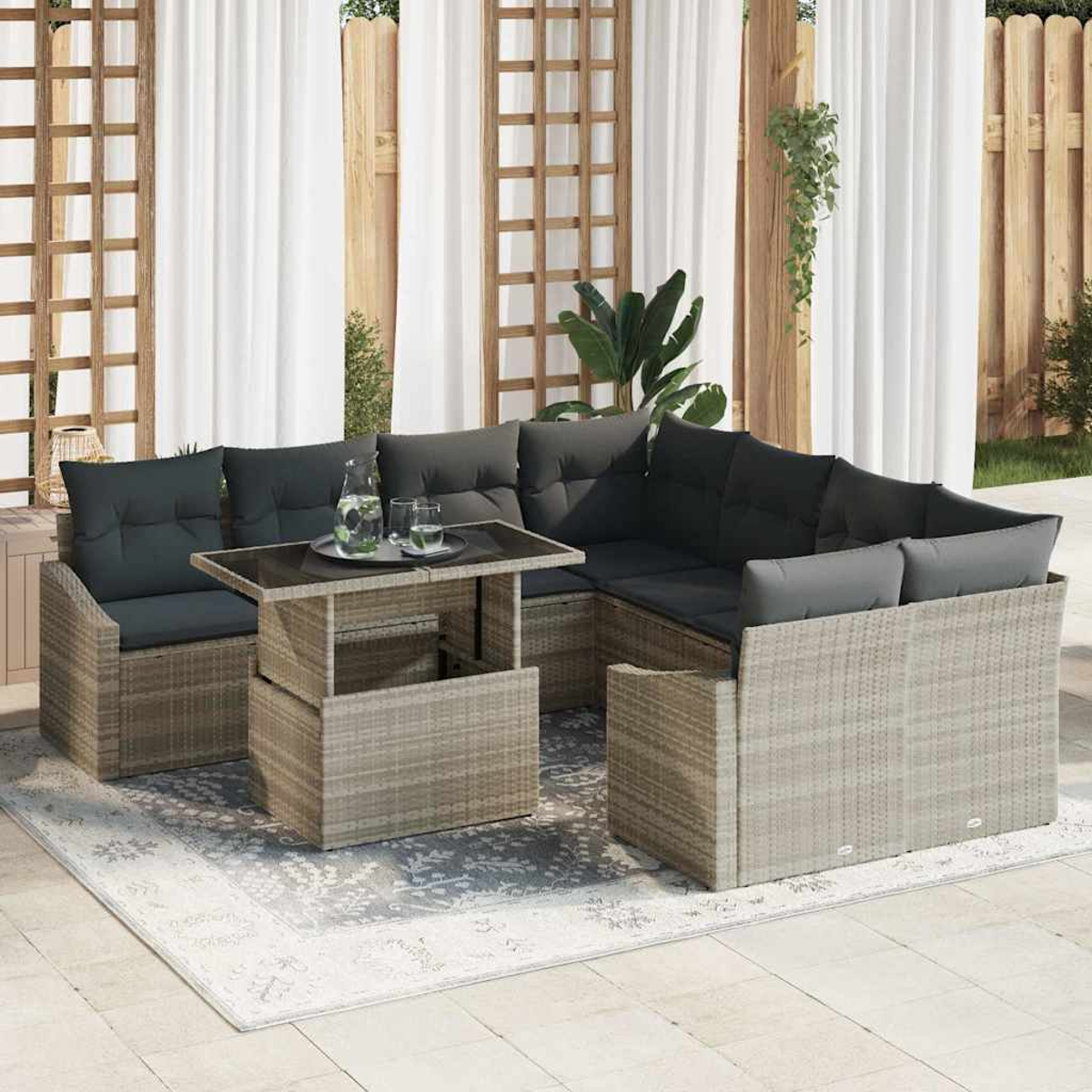 Outdoor-Ecksofa mit grauen Kissen und einem Tisch mit Glasplatte auf einem gemusterten Teppich, vor weißem Vorhang.