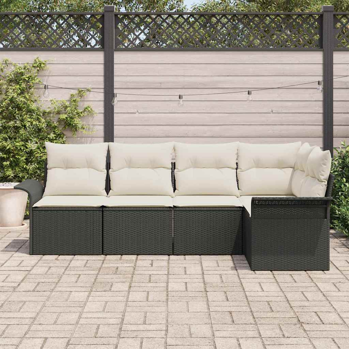 Outdoor-Ecksofa mit cremefarbenen Kissen auf einer Steinterrasse. Im Hintergrund ein Holzzaun und Grün.