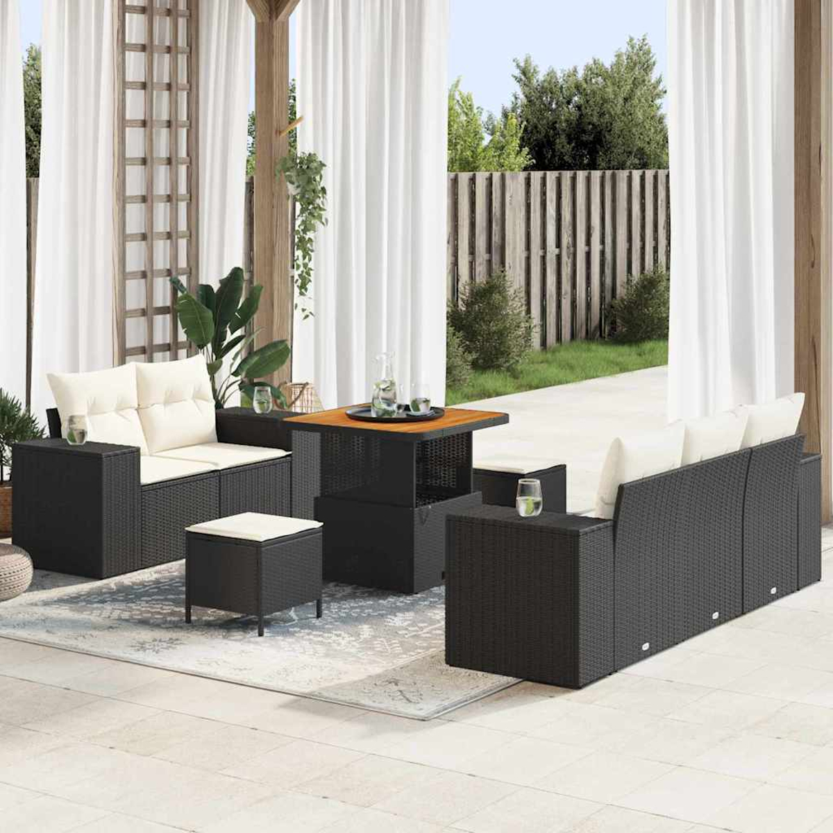 Terrassenmöbel-Set im Freien mit schwarzen Korbmöbeln, weißen Kissen, einem quadratischen Tisch und weißen Vorhängen. Pflanzen und ein Holzzaun im Hintergrund.