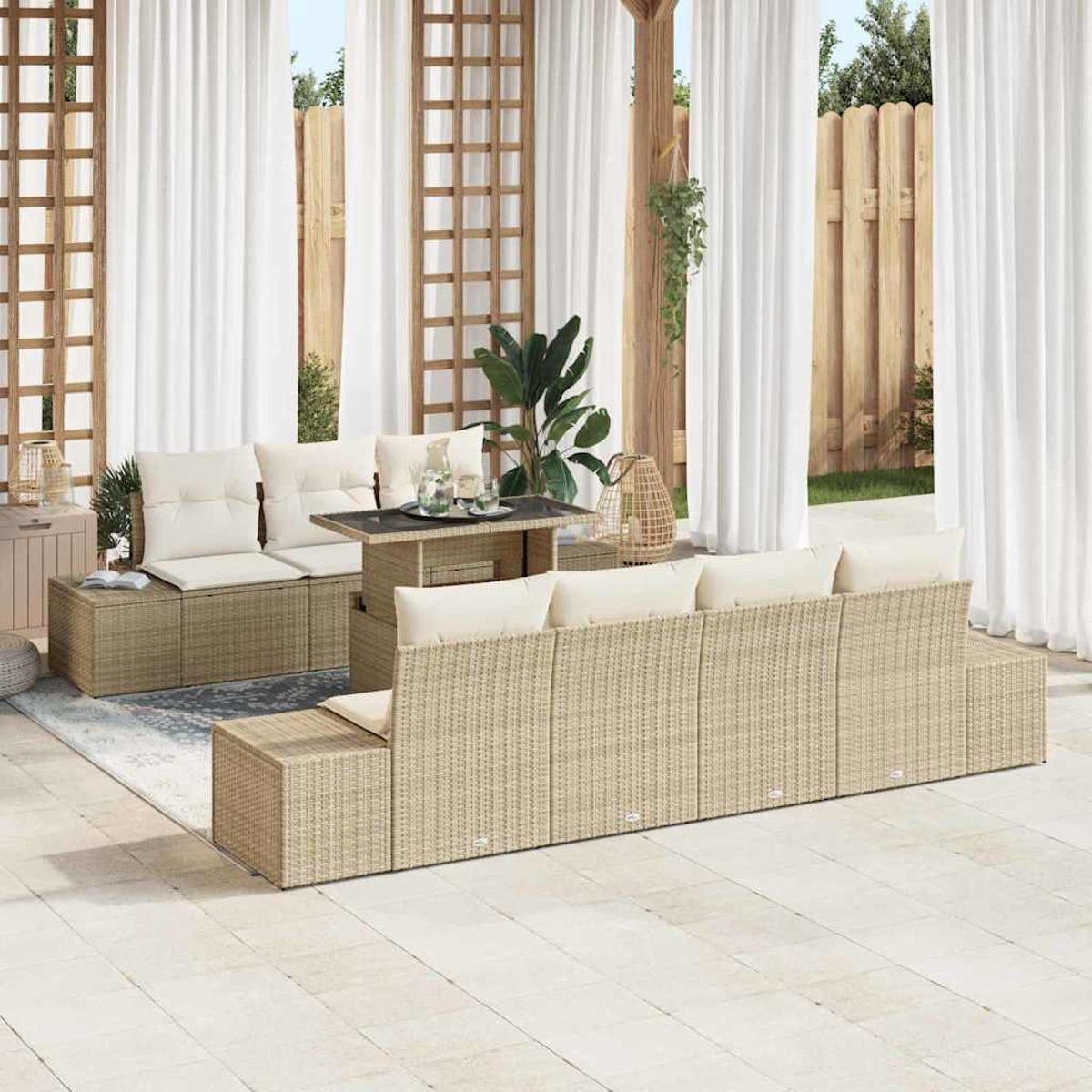 Garten-Terrassenset mit beigefarbenen gewebten Möbeln, weißen Kissen und einem kleinen Tisch. Weiße Vorhänge und Holzzaun im Hintergrund.